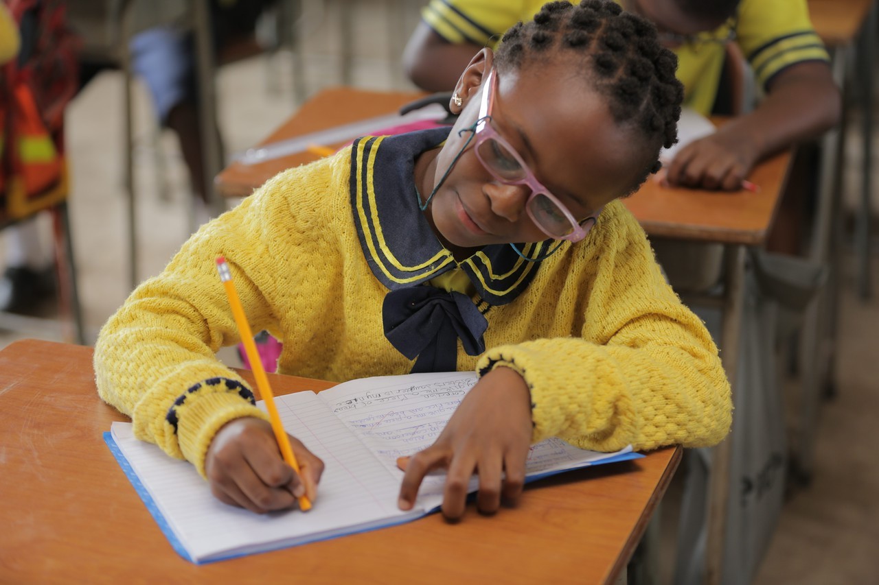 (c) Develop Africa—a Cameroonian girl in class writing in a book.