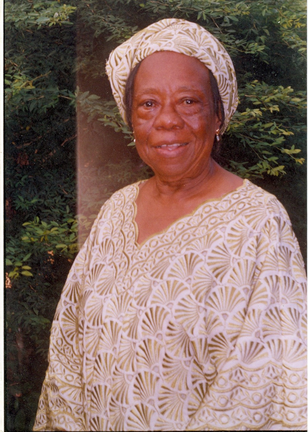 Zainabu Renner in a white and gold gown and head wrap, smiling